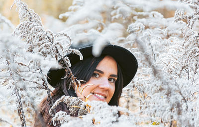 Portrait of smiling young woman in warm clothes and hat, plants, selective focus.