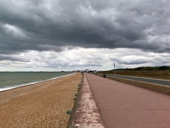 Road leading towards sea against cloudy sky