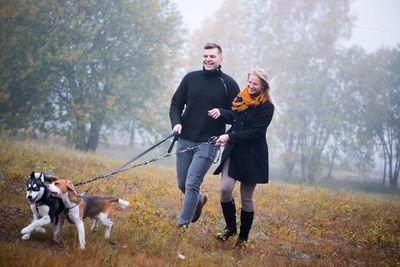 Young happy family couple walking with dog in misty autumn park