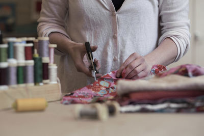 Midsection of woman cutting fabric on table at home