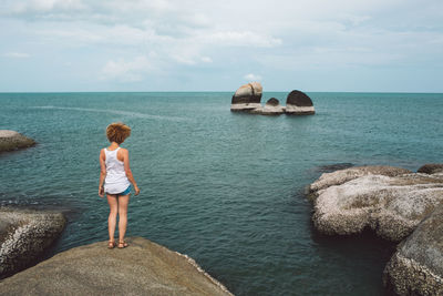 Rear view of woman standing on rock over sea against sky