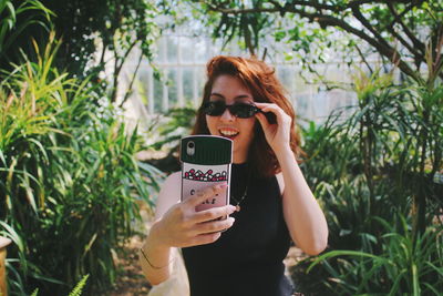 Woman using mobile phone while standing against plants