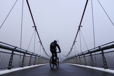 Man with bicycle on bridge against clear sky