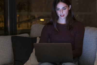 Young woman using laptop while sitting on sofa at home