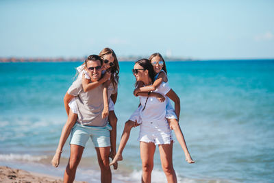 Parent piggybacking daughters while standing on beach