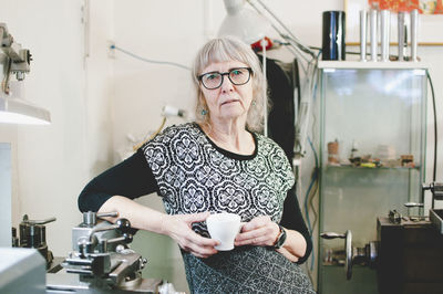 Portrait of confident senior woman holding coffee cup in jewelry shop