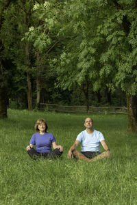 Vertical view of senior couple with eyes closed practising yoga in the park sorrounded by nature