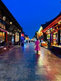 People walking on illuminated street amidst buildings in city at night