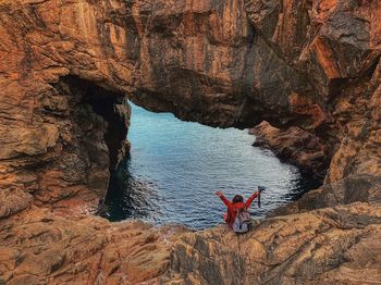 Rear view of woman sitting on rock formation at sea