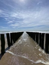 View of wooden posts in sea against sky