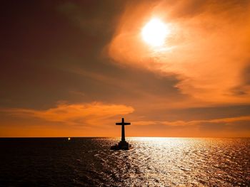 Silhouette lighthouse by sea against sky during sunset