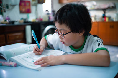 Rear view of boy holding book on table