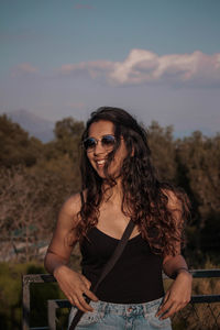 Portrait of smiling young woman wearing sunglasses against sky