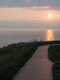 Footpath by sea against sky during sunset