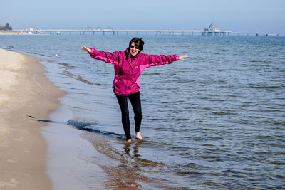 Full length of woman with arms outstretched standing at beach