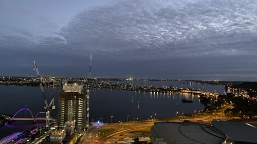 High angle view of illuminated city by sea against sky