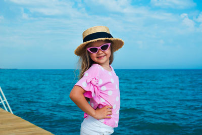 Funny face kid in sunglasses and straw hat posing on sea shore