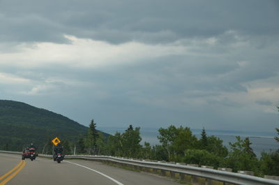 People riding bicycle on road against sky