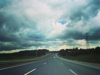 Empty road leading towards cloudy sky