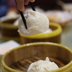 Close-up of person hand holding food with chopsticks over bamboo steamer