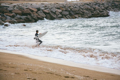 Man carrying surfboard while walking on shore at beach