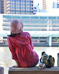 Rear view of woman sitting by river against building