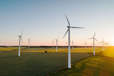 Wind turbines on grassy land against clear sky