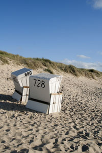 Hooded beach chairs on sand against clear blue sky