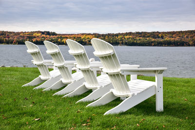 Row of chairs on lakeshore against sky