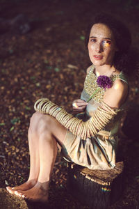 Portrait of woman holding flower while sitting in forest