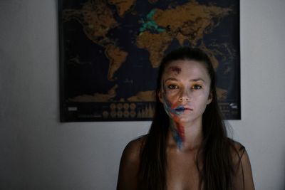 Portrait of young woman with messy make-up standing against wall at home