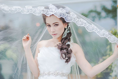 Portrait of bride wearing wedding dress standing at park