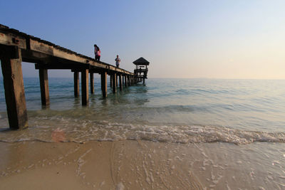 Low angle view of people on pier over sea against clear sky during sunset