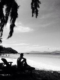 Rear view of man sitting on seat at beach against sky