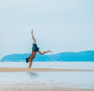 Full length of woman jumping on beach against sky
