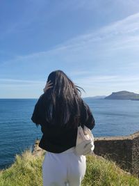 Rear view of woman sitting at beach against sky