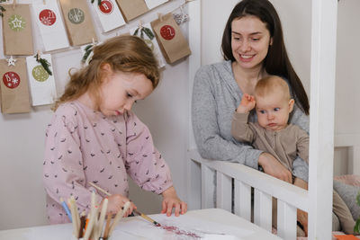 Mother spending time with two kids at home before christmas. looking photos in album, girl getting