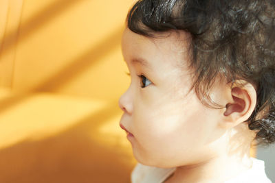 Close-up of cute baby girl looking away at home
