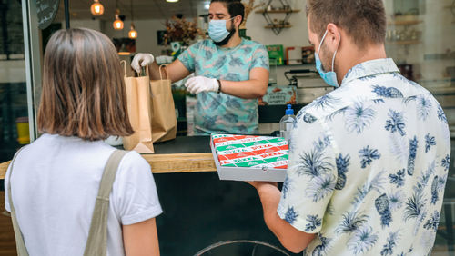 Owner giving pizza take away to customers at restaurant