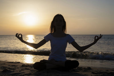 Full length of man sitting at beach during sunset