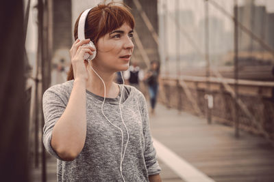 Woman listening to music while standing on bridge