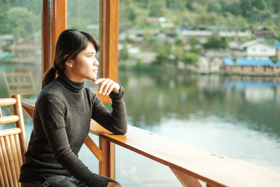 Side view of young woman looking away while sitting by railing