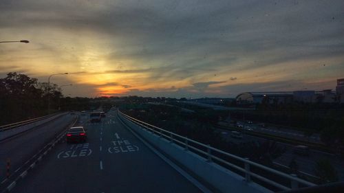 Vehicles on road against sky during sunset