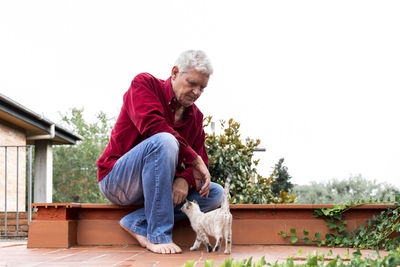 Senior man with kitten sitting on roof terrace