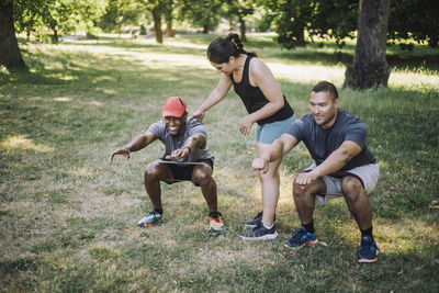 Female coach assisting men practicing squats on grass at park