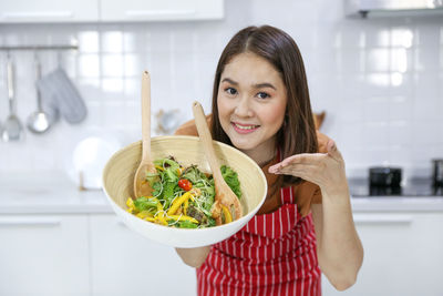 Portrait of a smiling young woman holding food at home