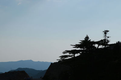 Silhouette trees and mountains against clear sky
