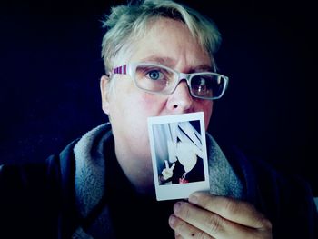 Close-up portrait of woman wearing eyeglasses holding instant print transfer