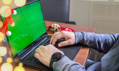 Man hands typing on laptop keyboard with empty green screen and christmas decoration on background. 