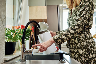 Woman pouring water from faucet into electric kettle at the kitchen